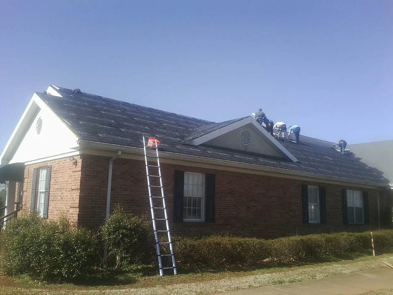 Crew tearing shingles off a brick ranch roof with a ladder set — Metal Roof Repair work by our crew in Peck