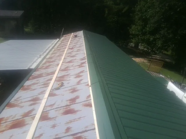 Old rusted panels beside newly installed green metal roofing — Wind Damage Roof Repair by Roofing Brothers in Peck